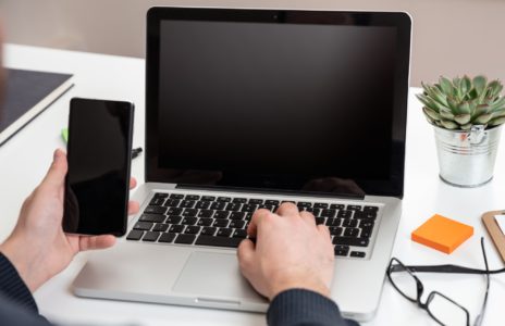 Laptop and smartphone with black blank screens, office interior background